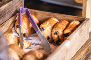Pan chocolate in a wooden crate with Furnace Kitchen branded greaseproof paper. There is a pair of purple handed pastry tongues in the centre of the picture.