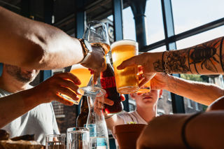 A close-up of a group of friends touching drinks glasses including wine, coca-cola and lager, together.