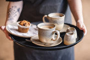 Two cups of coffee on a black tray with a muffin in the background.
